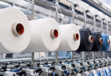 Sensormatic Solutions Expands Options For Sewn-in RFID Source Tagging Strategies Industrial textile production line featuring polyester yarn spools and modern spinning machinery representing global polyester price increases and shifts in apparel fibre sourcing.