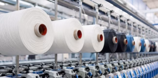 Industrial textile production line featuring polyester yarn spools and modern spinning machinery representing global polyester price increases and shifts in apparel fibre sourcing.