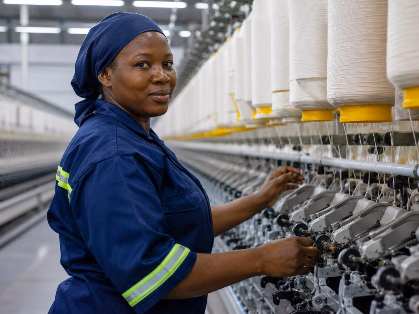 African textile factory worker operating spinning machinery, representing industrial growth, manufacturing capacity, and employment development across Africa.